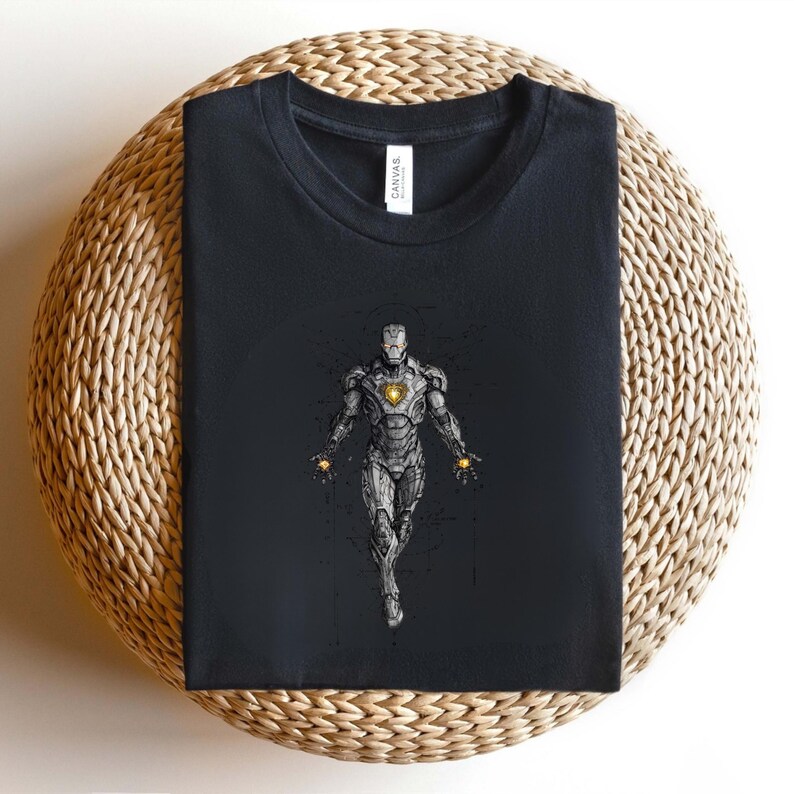 Op de afbeelding: Zwart t-shirt met een gedetailleerde illustratie van Iron Man. Het kunstwerk toont het metalen pantser van het personage, met een gloeiende boogreactor en handrepulsors. Het t-shirt is op een geweven oppervlak gevouwen.