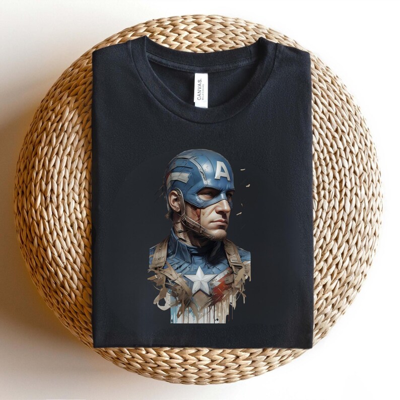 May include: Black t-shirt featuring a detailed illustration of Captain America. The design showcases Captain America's helmet, uniform, and a star emblem. The shirt is folded on a woven surface.