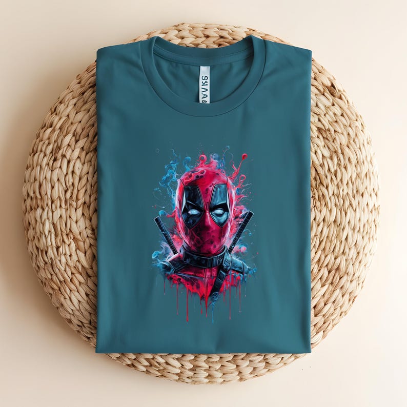May include: Teal t-shirt featuring a vibrant graphic of Deadpool's face. The artwork showcases Deadpool's mask with red and black details, surrounded by blue and red artistic smoke effects. Two katanas are crossed behind the head.