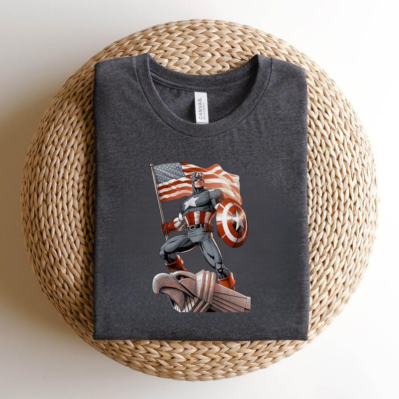 Pode incluir: T-shirt cinza escuro com um gr&aacute;fico do Capit&atilde;o Am&eacute;rica segurando uma bandeira americana e um escudo. O design inclui o ic&ocirc;nico escudo estrelado e as cores vermelha, branca e azul da bandeira. A camisa &eacute; feita de um material macio.
