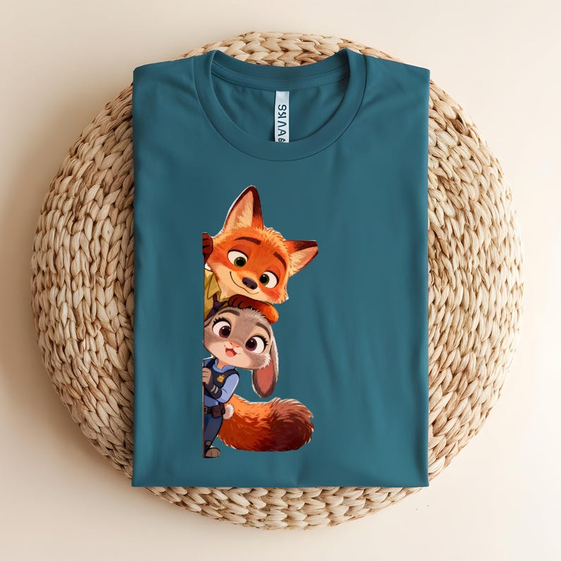May include: A teal crew neck t-shirt featuring a graphic print of a cartoon fox and a cartoon rabbit peeking out from the side. The fox has orange fur and the rabbit has gray fur and is wearing a blue uniform. The shirt has a white neck label.