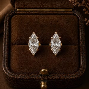 Puede incluir: Un par de pendientes de botón con piedras transparentes de talla marquesa engastadas en metal dorado. Cada piedra está asegurada por varias garras, creando una forma puntiaguda y alargada. Los pendientes se presentan en un joyero de terciopelo marrón.