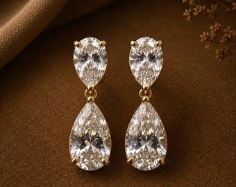 May include: A pair of gold drop earrings featuring two clear pear-shaped stones each. The top stone is smaller and connected to a larger pear-shaped stone below by a small gold link. The stones are faceted and set in gold prongs.