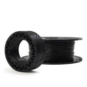 Puede incluir: Bobina de filamento negro para impresora 3D y un objeto negro con forma de neumático. El filamento está enrollado firmemente en una bobina negra. El objeto con forma de neumático tiene un diseño estampado y un centro hueco.