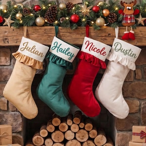 May include: Four personalized Christmas stockings in tan, teal, red, and white velvet. Each stocking features a white cuff with a ruffled edge and embroidered names Julian, Hailey, Nicole, and Dustin in matching thread colors.