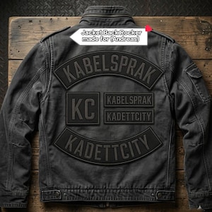 May include: A dark grey denim jacket featuring several patches. The patches display the text "KABELSPRAK", "KC", "KADETTCITY", and "KABELSPRAK KADETTCITY". The jacket has a zip closure and a collar. The text "Jacket Back Rocker made for (Andreas)" is also visible.