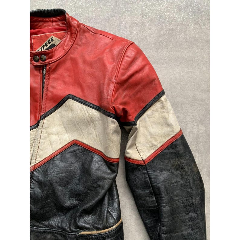 May include: A vintage leather motorcycle jacket in red, black, and cream. The jacket features a stand-up collar, a zipper closure, and a color-block design with chevron accents. The brand name is visible on the collar.