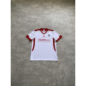 Op de afbeelding: Wit Adidas voetbalshirt met rode accenten op de mouwen en zijkanten. Het shirt toont de tekst "TEAM 2011" en een Duits vlagembleem. Gemaakt van lichtgewicht, ademend materiaal.