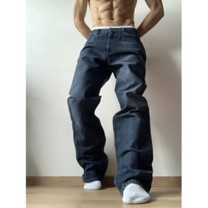 Könnte beinhalten: Dunkelblaue Jeans mit entspannter Passform. Die Jeans haben ein klassisches Fünf-Taschen-Design und ein gerades Bein. Das Model trägt weiße Socken. Ein vielseitiges Kleidungsstück.
