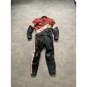May include: A vintage motorcycle racing suit in black, red, and white leather. The one-piece suit features a zip-up front, padded knees, and a classic racing design. The suit is a size medium.