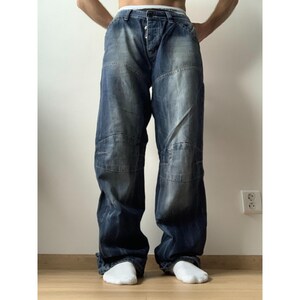 May include: Dark wash denim jeans with a relaxed fit. The jeans feature a button fly and reinforced knee panels. The denim has a faded, worn look. The jeans are paired with white socks.