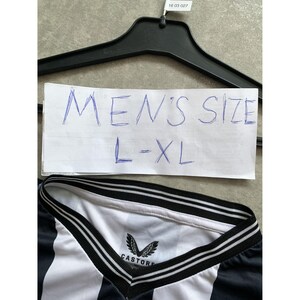 May include: A black and white striped shirt with a V-neck collar featuring black and white trim. The interior neck label displays the Castore brand logo and name. A white paper sign above the shirt displays the handwritten text MEN'S SIZE L-XL.