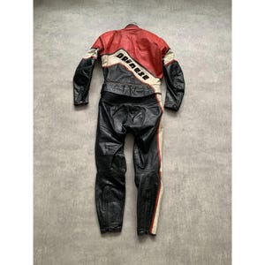 May include: A black, red, and white leather motorcycle racing suit. The suit features a red upper section with white and black accents, and the brand name "Dainese" is prominently displayed. The lower section is black with white and red stripes.
