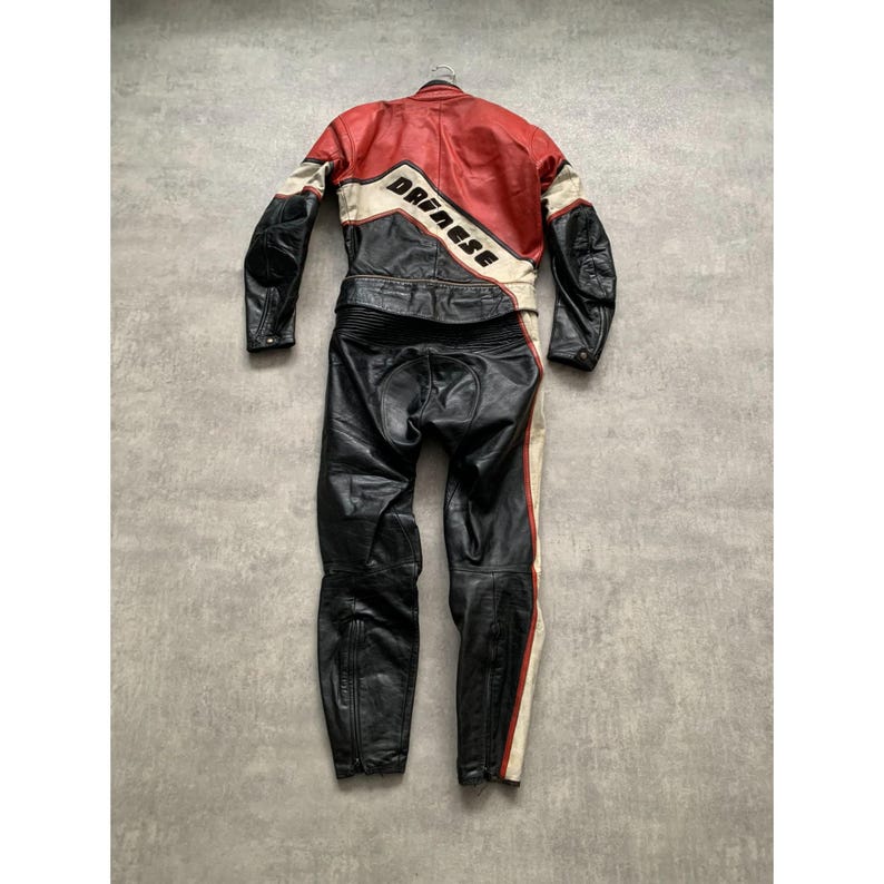 May include: A black, red, and white leather motorcycle racing suit. The suit features a red upper section with white and black accents, and the brand name "Dainese" is prominently displayed. The lower section is black with white and red stripes.