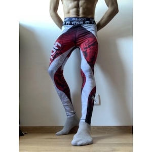 Peut inclure: Legging de compression avec un motif rouge, blanc et noir. Le legging présente le mot "Venum" en blanc et un motif. La ceinture porte les inscriptions "LYLE & SCOTT" et "Venum".