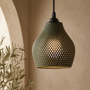 Pode incluir: Uma luminária pendente com uma cúpula em forma de sino com uma estrutura de treliça verde-oliva em padrão de diamante. A cúpula é suspensa por um cabo escuro e uma tampa preta, com uma luz quente brilhando através do design de malha.