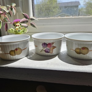 May include: Three white ceramic ramekins with fluted sides. The two outer ramekins feature a graphic of two green olives on a toothpick. The center ramekin features a graphic of a cluster of dark purple blackberries with green leaves.