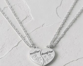 May include: A silver-colored necklace set featuring two heart-shaped pendants that connect to form a whole. One pendant is inscribed with "mother," the other with "daughter." Each pendant has a decorative swirl design.