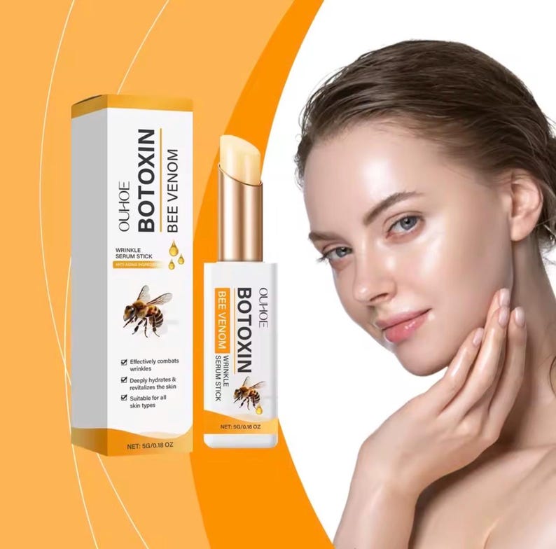 May include: A white and gold Ouhoe Botoxin Bee Venom wrinkle serum stick in a matching rectangular box. The packaging features a bee illustration, the product name, and the net weight of 5g/0.18 oz. The stick has a twist-up mechanism.