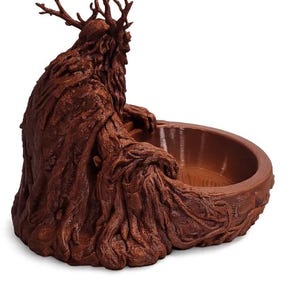 May include: A brown, textured bowl featuring a sculpted figure with a tree-like appearance. The figure has branch-like antlers and a flowing, bark-textured cloak that extends to form the circular basin of the bowl, creating a unified, organic structure.
