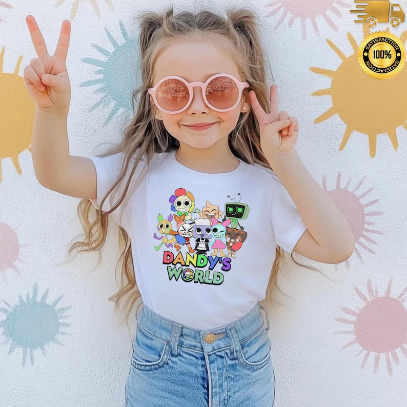 Może przedstawiać: Biała koszulka z kolorową grafiką z kresk&oacute;wek i napisem "Dandy's World". Grafika zawiera r&oacute;żne postacie z kresk&oacute;wek. Osoba na zdjęciu ma na sobie niebieskie dżinsy i r&oacute;żowe okulary przeciwsłoneczne.
