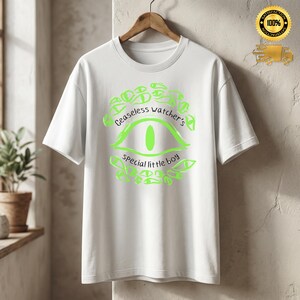Puede incluir: Camiseta blanca con un dise&ntilde;o de ojo verde ne&oacute;n y el texto "Ceaseless watcher's special little boy". El dise&ntilde;o presenta un ojo en el centro, rodeado de ojos m&aacute;s peque&ntilde;os y texto. La camiseta est&aacute; colgada en una percha de madera.