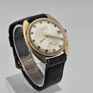May include: A vintage Longines Ultra-Chron automatic wristwatch with a gold-tone case, a round off-white dial, gold-tone hour markers and hands, a date window at the three o'clock position, and a black leather strap with a metal buckle.