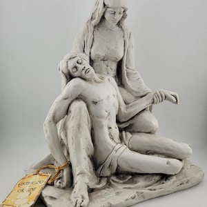 Pode incluir: Uma escultura branca que retrata uma mulher segurando um homem. O homem está deitado e a mulher está sentada atrás dele. A escultura tem uma etiqueta que diz "CERTIFICATO DI ORIGINE".