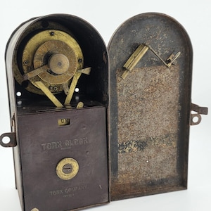 May include: A vintage Tork Clock time switch in a dark brown metal housing with an open hinged door. The device features a brass circular dial with numerical markings, a central knob, and the text TORK CLOCK and TORK COMPANY embossed on the front.