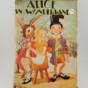 May include: A vintage hardcover book titled Alice in Wonderland featuring a color illustration of Alice, a rabbit, and the Mad Hatter on the front cover. The cover shows signs of wear along the edges and includes a small white circular sticker with the number 17.