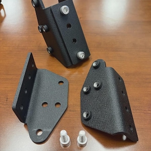 Pode incluir: Três suportes de metal pretos com vários orifícios e parafusos prateados. Um suporte está em pé, enquanto os outros dois estão angulados. Dois parafusos prateados também estão presentes. Os suportes têm um acabamento texturizado.