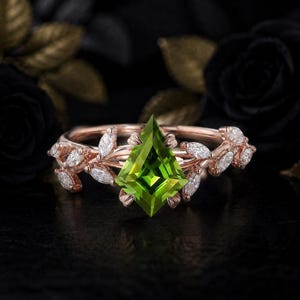 Könnte beinhalten: Ein Ring aus Roségold mit einem drachenförmigen grünen Peridot als Mittelstein. Die Ringschiene ist mit einem rankenartigen Motiv gestaltet und mit kleinen, im Marquise-Schliff geschliffenen weißen Diamanten in Blattform an den Seiten verziert.
