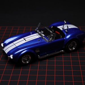 May include: A blue toy car with white racing stripes. The miniature vehicle has a sleek design, chrome accents, and a black interior. The car is a classic sports car model.