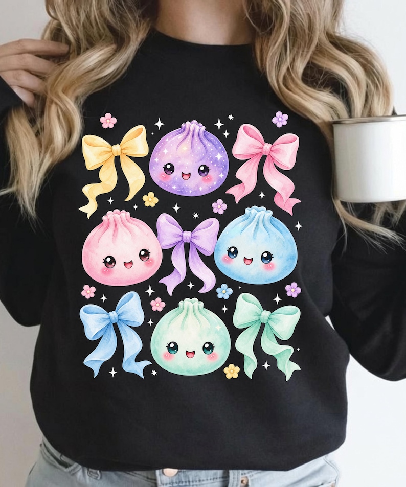 May include: A black long-sleeve sweatshirt featuring a graphic print of four colorful, smiling dumpling characters in purple, pink, blue, and mint green, interspersed with five pastel-colored bows and small floral accents and stars.