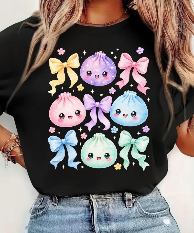 May include: A black t-shirt featuring a graphic print of four smiling, round, pastel-colored dumplings in purple, pink, blue, and mint green, interspersed with five colorful bows in yellow, pink, purple, blue, and mint green, plus small flowers.