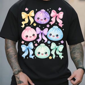 May include: A black short-sleeved t-shirt featuring a graphic print of four pastel-colored, smiling dumpling characters in purple, pink, blue, and mint green, interspersed with various colored ribbons and small flower accents.