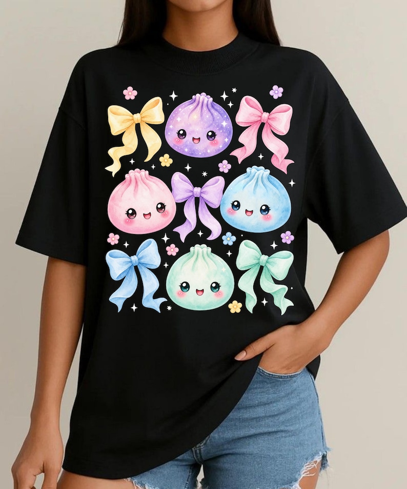 May include: A black short-sleeved t-shirt featuring a graphic print of four colorful, smiling dumpling characters in purple, pink, blue, and mint green, surrounded by pastel-colored ribbons, small flowers, and sparkling star accents.