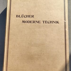 May include: A vintage book with a tan cover and the title "BLÜCHER MODERNE TECHNIK" in brown text. The book has a brown border and appears to be in good condition, with slight wear on the edges. The overall aesthetic suggests a historical or technical theme.