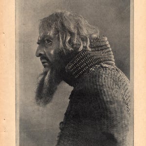 Op de afbeelding: Een zwart-wit portret van een man in profiel, met een lange baard en krullend haar. Hij draagt een maliënkolder. De afbeelding komt uit een vintage publicatie, met tekst boven en onder.