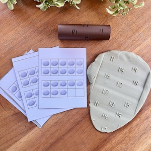 May include: A collection of educational tools for learning. Includes a brown cylinder with "PI" and "II" markings, several white cards with oval shapes, and a green clay shape with numbers.