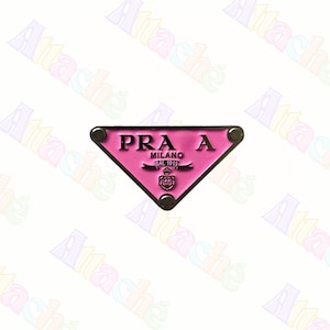 May include: A pink triangular emblem with the text "PRA A MILANO DAL 1913" in black. The emblem has a silver border and is set against a white background. The emblem is a fashion accessory.