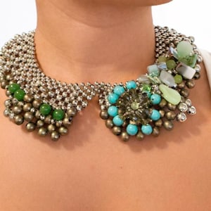 Puede incluir: Un collar llamativo con dise&ntilde;o de cuello. El collar est&aacute; compuesto por cuentas plateadas, piedras verdes y turquesas, y cristales transparentes. El dise&ntilde;o incorpora una mezcla de texturas y colores, creando un accesorio audaz y llamativo.