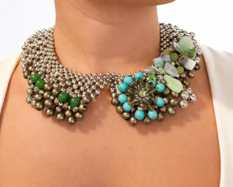 Puede incluir: Un collar llamativo con dise&ntilde;o de cuello. El collar est&aacute; compuesto por cuentas plateadas, piedras verdes y turquesas, y cristales transparentes. El dise&ntilde;o incorpora una mezcla de texturas y colores, creando un accesorio audaz y llamativo.