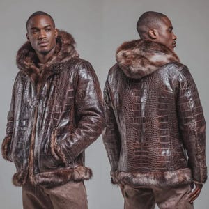 Puede incluir: Chaqueta de cuero marrón con capucha y ribete de piel sintética. La chaqueta tiene una textura de piel de cocodrilo y cuenta con cierre de cremallera y bolsillos. El modelo lleva pantalones marrones.