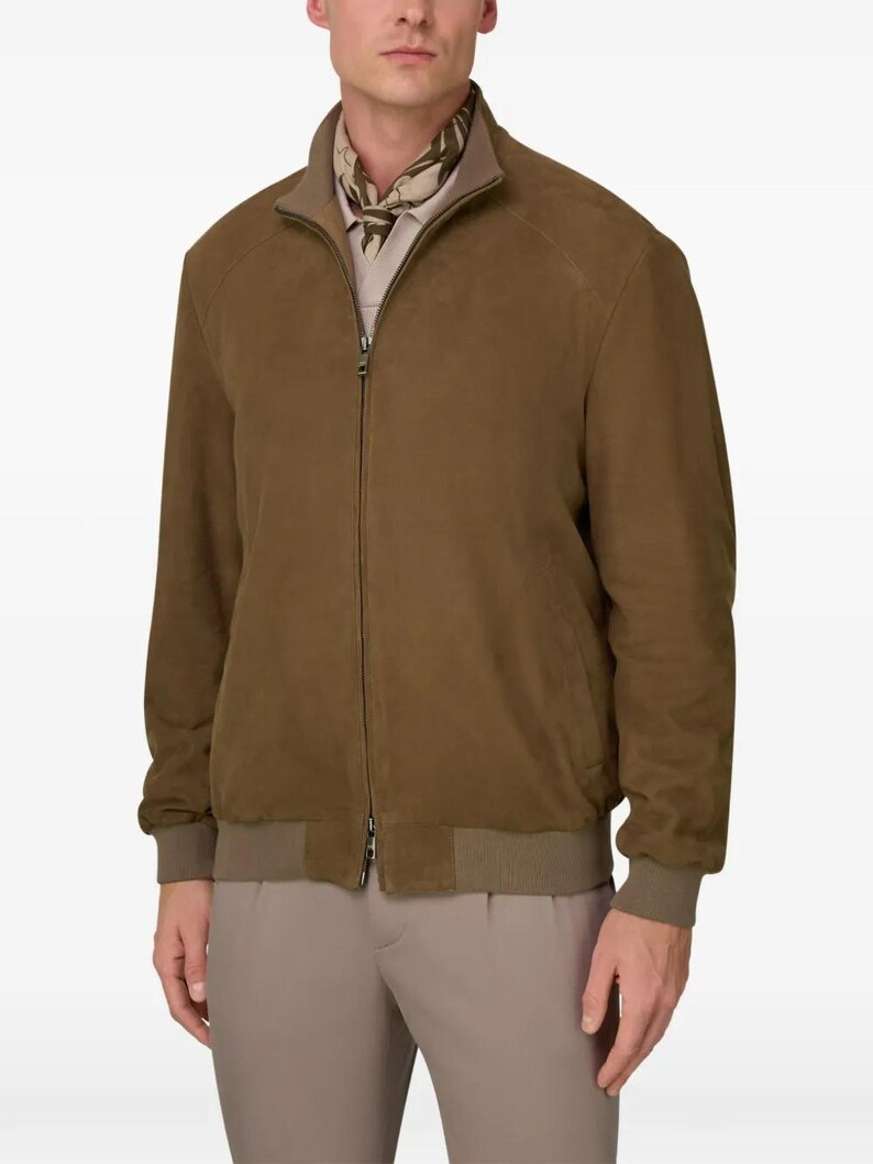 Peut inclure: Veste de bombardier en daim marron avec fermeture &eacute;clair, poignets et ourlet c&ocirc;tel&eacute;s assortis. La veste a un col montant et une doublure marron clair. Le mod&egrave;le porte une chemise et un pantalon marron clair.
