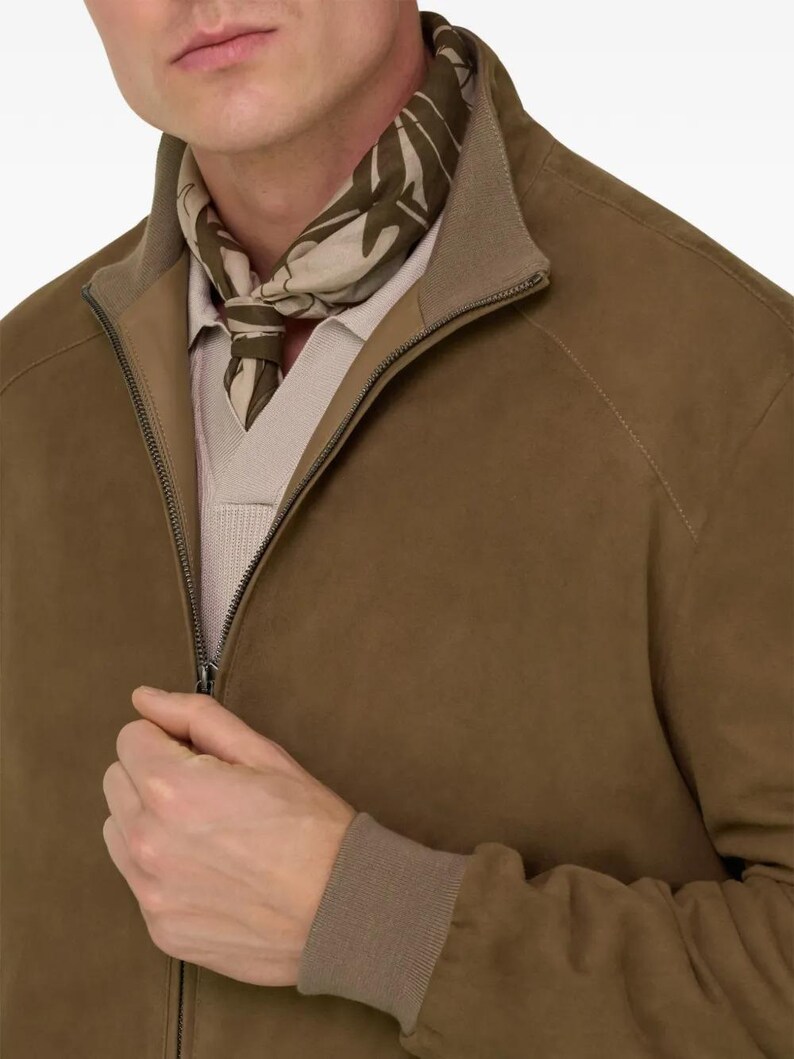 Peut inclure: Veste en daim marron avec fermeture &eacute;clair et col marron clair. La veste est associ&eacute;e &agrave; une &eacute;charpe &agrave; motifs dans les tons verts et beiges. Le mod&egrave;le porte une chemise beige clair sous la veste.