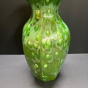 May include: A ceramic vase featuring a vibrant green glaze with a crystalline pattern. The surface displays a glossy finish with lighter green and white circular crystal formations scattered across the body, which has a flared rim and a tapered base.