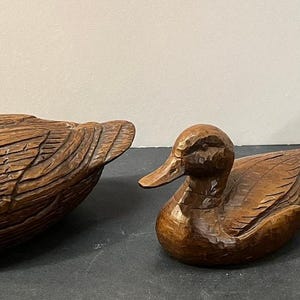 May include: Three hand-carved wooden duck figurines of varying sizes, each featuring a polished dark brown finish with visible chisel marks and detailed feather textures on the wings, heads, and bodies, arranged in a horizontal line.