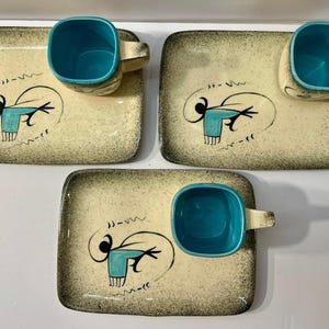 May include: Three rectangular ceramic snack sets, each featuring a cream-colored tray with a speckled brown border and a matching cup with a vibrant turquoise interior. Each tray displays a black abstract line drawing of a stylized figure.