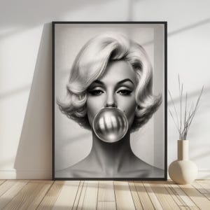 May include: Black and white framed print of a woman with platinum blonde hair blowing a large, metallic bubble. The portrait is a close-up, focusing on the woman's face and the bubble. The print is displayed on a wooden floor.
